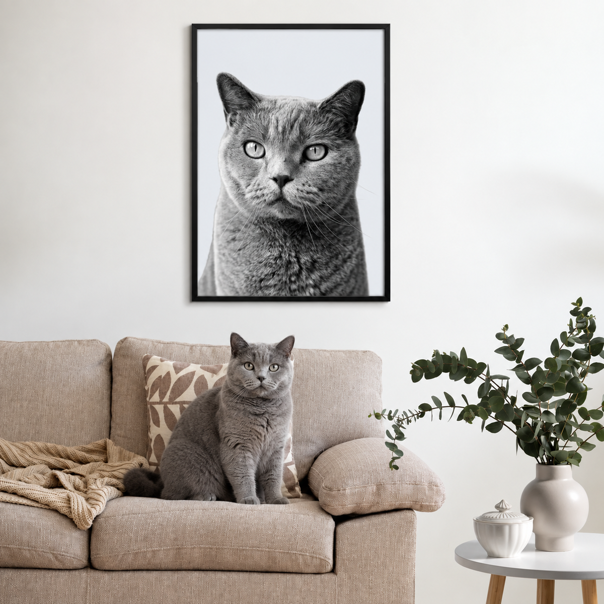 Portrait d'animal gris encadré au-dessus d'un canapé beige avec un chat gris semblable devant.