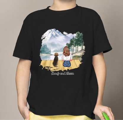 T-shirt enfant noir avec illustration d'une fille et d'un chien au bord d'un lac, montagnes en arrière-plan.