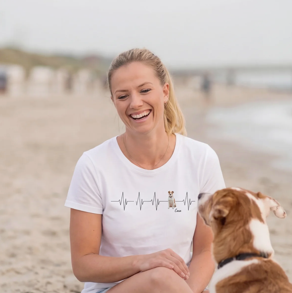 T-shirt blanc avec motif battement de cœur et chien, femme assise sur la plage.