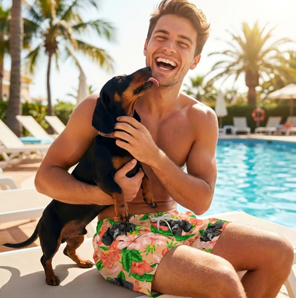 Homme avec chien noir assis au bord de la piscine, portant un short de bain coloré à motif de fleurs et de chiens.