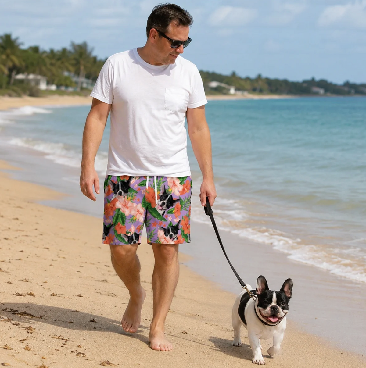 Homme portant un short de bain personnalisé à motif coloré de fleurs et d'animaux, marchant pieds nus sur la plage.