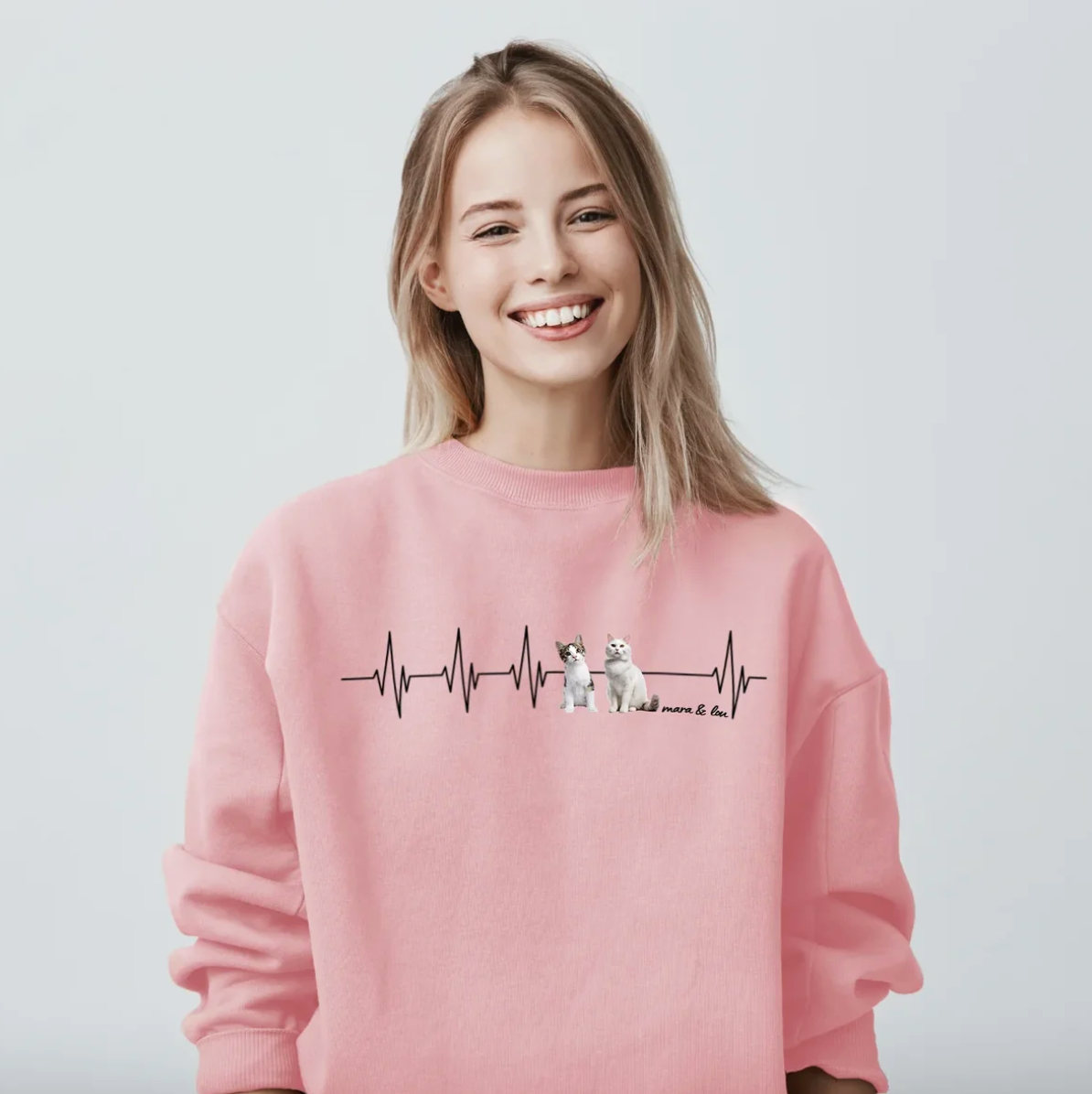Sweat-shirt rose avec motif battement de cœur et illustrations d'animaux. La personne sourit.