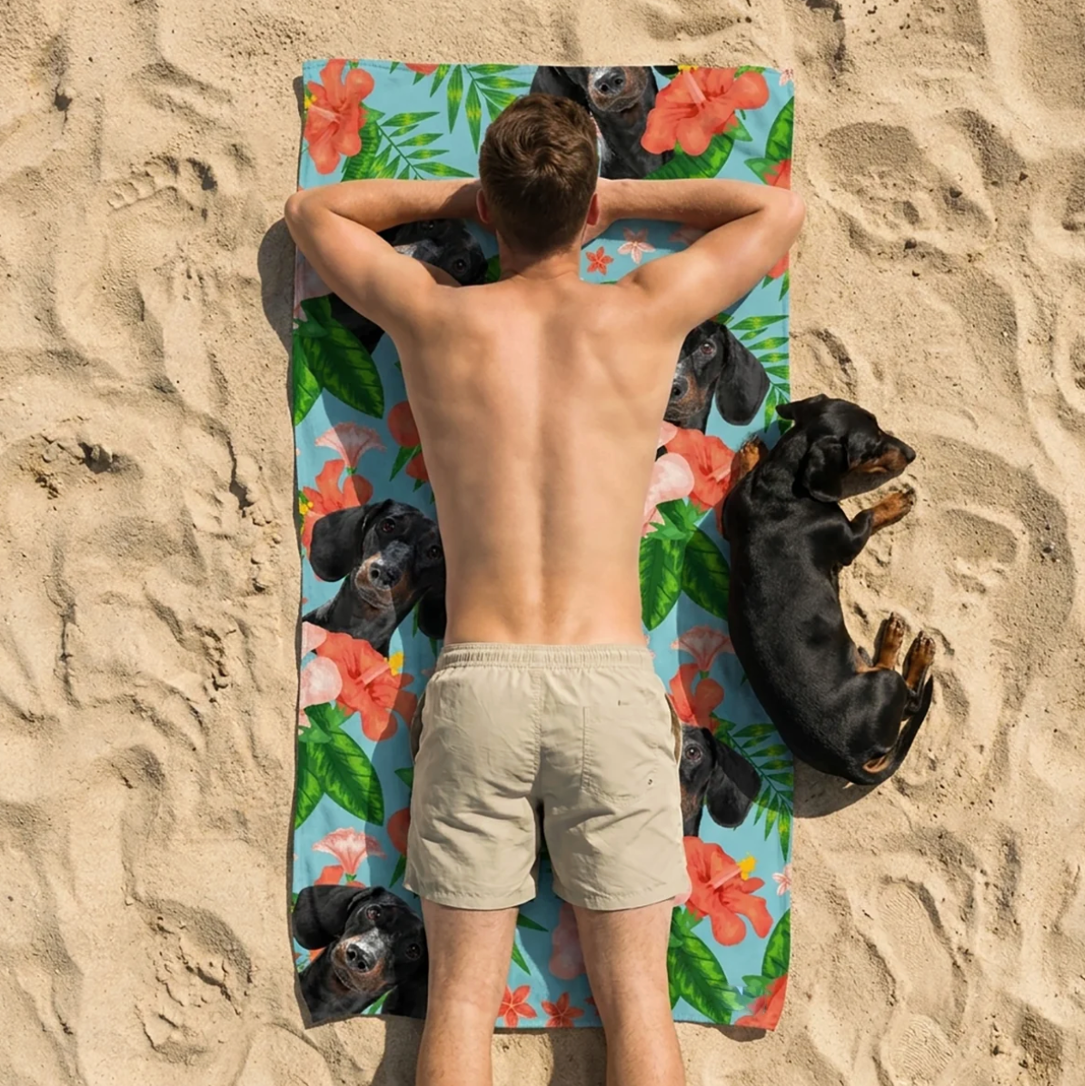 Personne allongée sur une serviette de plage personnalisée à motifs de chiens, entourée de sable.