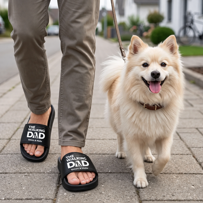 Personne portant des claquettes noires personnalisées avec l'imprimé "THE WALKING DAD", promenant un chien.